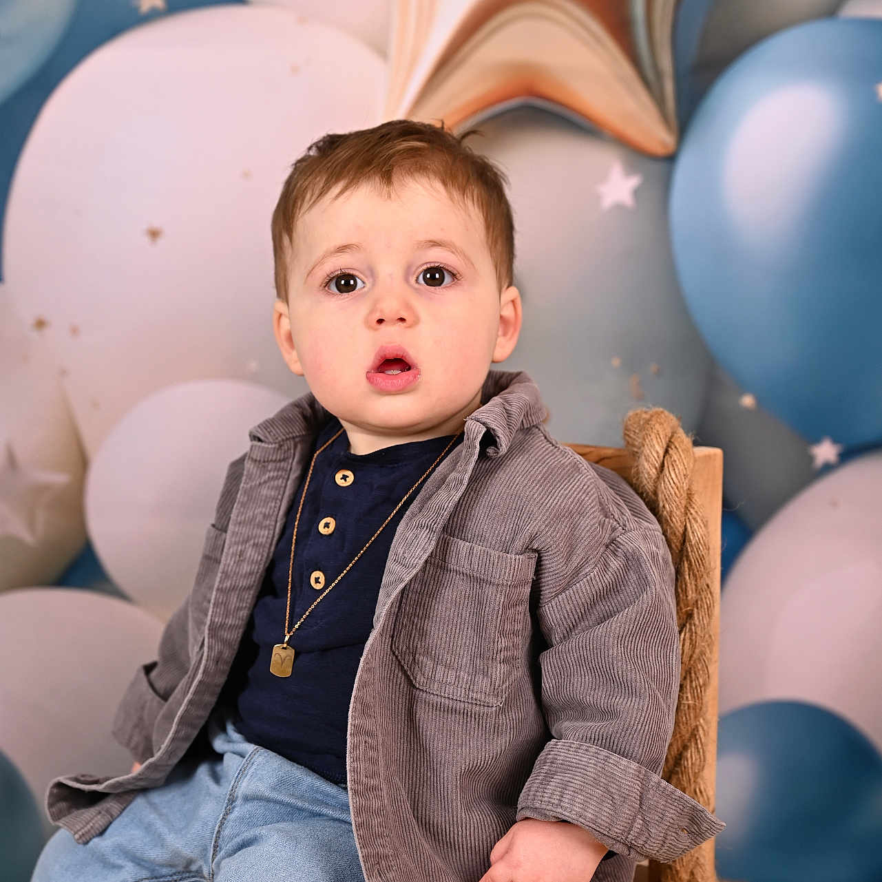 Noé participe au concours pour gagner de l'argent avec cette photo : toddler, child, boy, chair, rope, jacket, jeans, balloons, stars, background, portrait, indoor, casual_clothing, expression, seated, wooden_furniture, cute, celebration, decor, young_child
