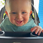 Kaden is registered to the contest to win money with this photo: baby, child, smiling, blue_eyes, stroller, graco, happy, outdoor, greenery, blue_wall, hands, clothing, seatbelt, portrait, infant, cute, sunlight, face, person, baby_toy_tray