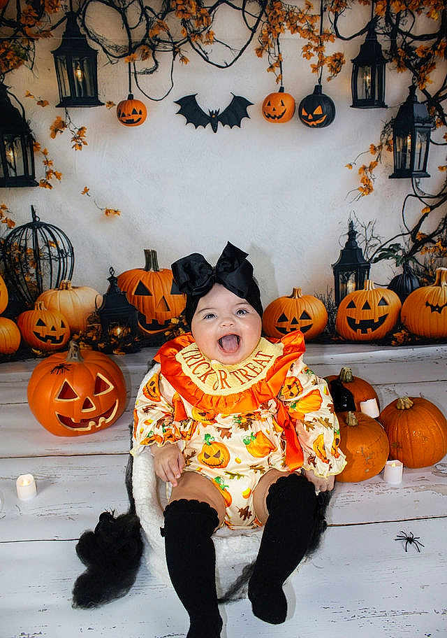 Alarni-Mae joined the competition — help win amazing prizes! autumn_leaves, baby, black_bow, black_socks, celebration, child, costume, cute, decorations, festive, halloween, holiday, indoors, jack_o_lantern, lantern, orange, pumpkin, sitting, smiling, spooky