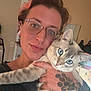 Bean is registered to the contest to win money with this photo: person, cat, glasses, blue_eyes, tattoo, indoor, holding, butterfly_patch, sweater, face, hand, piercing, nose_ring, ear_gauges, feline, pet, closeup, portrait, animal, cozy