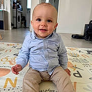 Liam participe au concours pour gagner de l'argent avec cette photo : baby, child, smiling, sitting, play_mat, shirt, pants, indoor, home, floor, face, person, curly_hair, happy, toy, modern, clean, appliance, robot_vacuum, washing_machine
