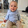 baby, child, smiling, sitting, play_mat, shirt, pants, indoor, home, floor, face, person, curly_hair, happy, toy, modern, clean, appliance, robot_vacuum, washing_machine