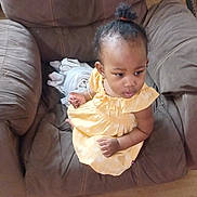Stephanie is registered to the contest to win money with this photo: toddler, child, yellow_dress, armchair, brown_furniture, curly_hair, indoors, cushion, blanket, portrait, seated, looking_away, young_child, comfortable, home_interior, casual, baby, small_child, person, cute