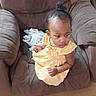 toddler, child, yellow_dress, armchair, brown_furniture, curly_hair, indoors, cushion, blanket, portrait, seated, looking_away, young_child, comfortable, home_interior, casual, baby, small_child, person, cute