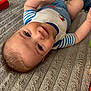 baby, child, infant, smiling, lying_down, blue_clothing, striped_shirt, shorts, blanket, indoor, person, cute, happy, skin, head, face, hand, foot, young, playful