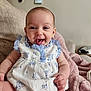 baby, smiling, dress, blue, white, couch, blanket, happy, tongue_out, indoor, child, person, cute, sitting, infant, furniture, soft, cozy, portrait, home