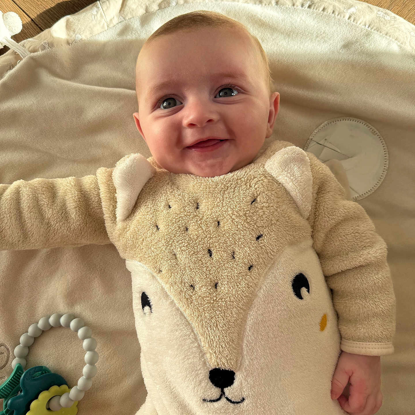 Léo a rejoint le concours — aidez-le/la à gagner de superbes lots ! animal_design, baby, blanket, child, cute, eyes, face, fleece, hand, happy, indoor, infant, lying_down, portrait, smile, soft_texture, teething_ring, toy, warm_light, wood_floor