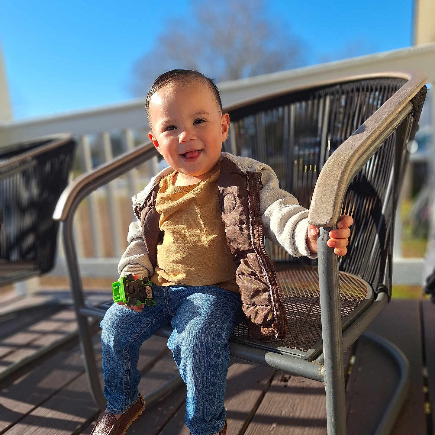 Dereck Sagastume is registered to the contest to win money with this photo: blue_sky, blurred_background, brown_shoes, casual_clothing, child, daytime, happy, jacket, jeans, metal_chair, outdoor, patio_chair, person, playtime, sitting, smiling, sunlight, toddler, toy_car, wooden_deck