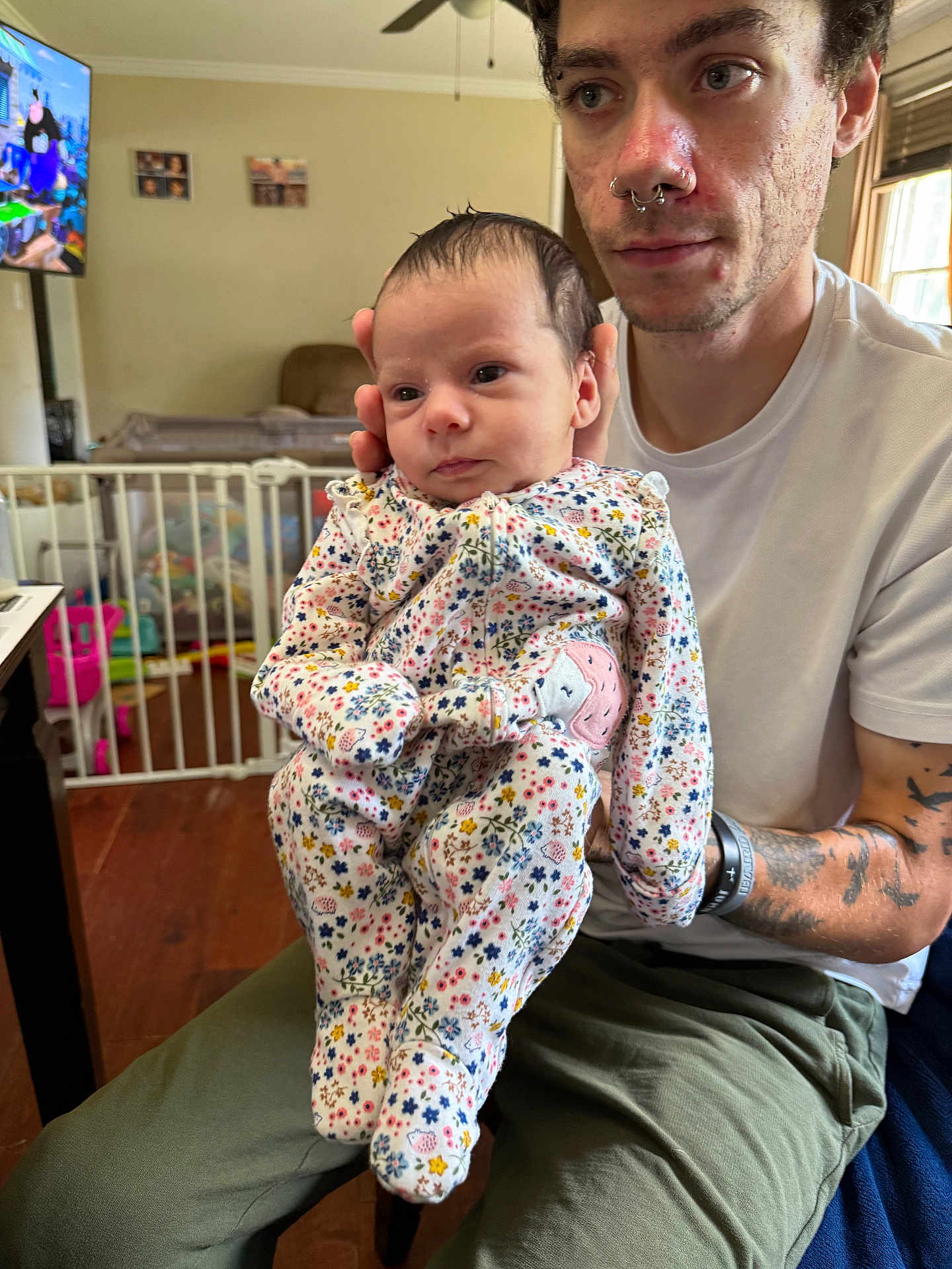 Amylia joined the competition — help win amazing prizes! baby, adult, person, floral_clothing, tattoos, piercings, living_room, baby_gate, television, cartoon, wooden_floor, window, curtains, seated, holding, face, expression, hand, casual_clothing, indoor