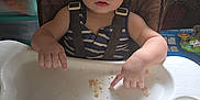 Lucas joined the competition — help win amazing prizes! toddler, child, high_chair, curly_hair, snack, food, indoor, person, baby_supplies, plant, table, seat, clothing, straps, messy, curious, expression, hand, face, room
