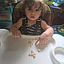 toddler, child, high_chair, curly_hair, snack, food, indoor, person, baby_supplies, plant, table, seat, clothing, straps, messy, curious, expression, hand, face, room