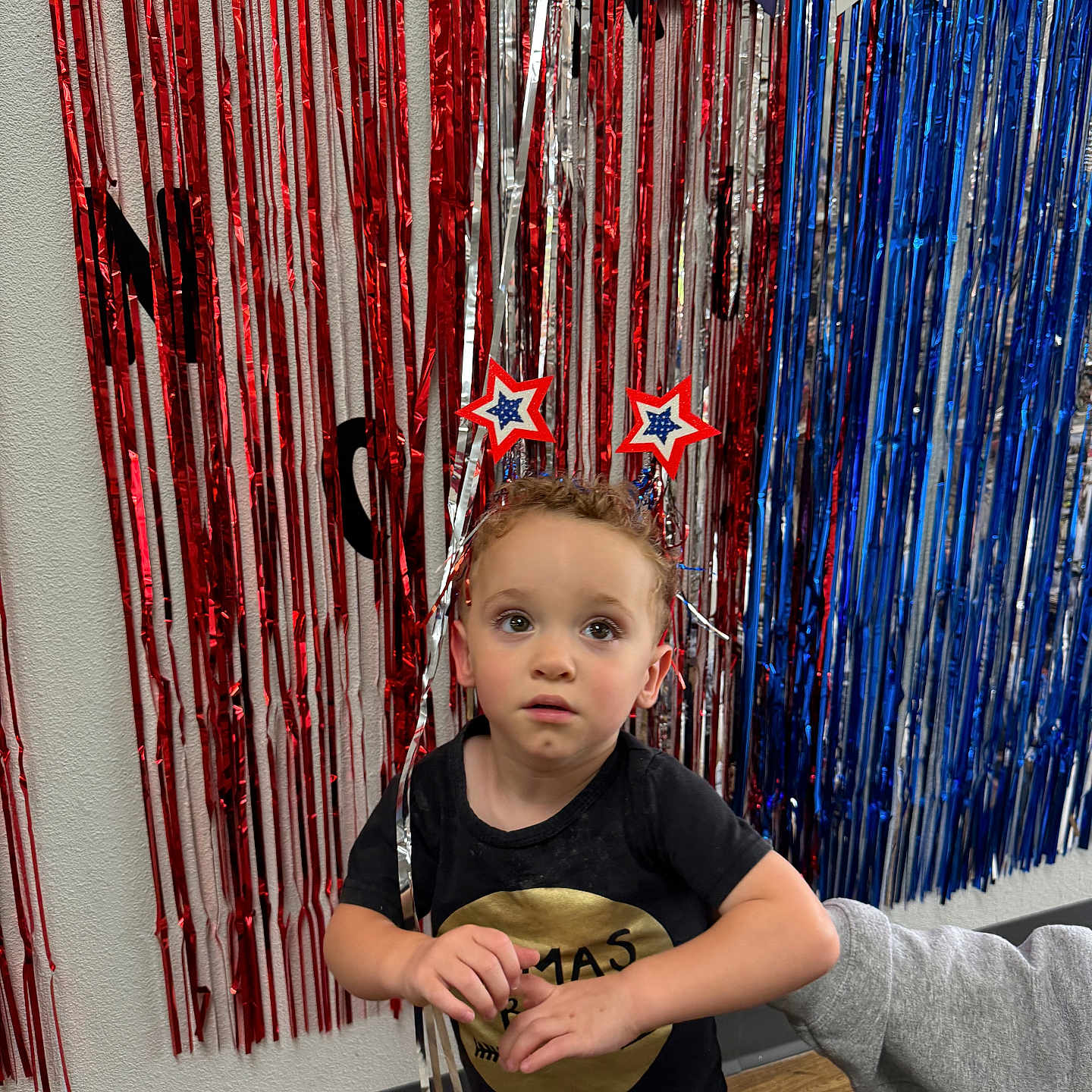 Hansel is registered to the contest to win money with this photo: blue, boy, celebration, child, curly_hair, decorations, festive, floor, hand, headband, indoor, party, person, red, shirt, stars, support, toddler, wall, white