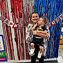 Hansel joined the competition — help win amazing prizes! banner, blue, celebration, clothing, curious, decorations, festive, floor, footwear, headband, holding, indoor, party, red, smiling, streamers, toddler, wall, white, woman