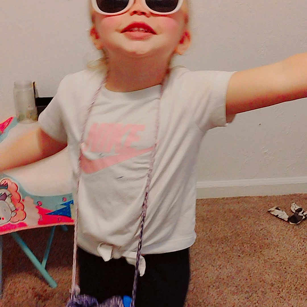 Briasia is registered to the contest to win money with this photo: accessory, bag, blonde_hair, carpet, child, cute, fashion, floor, hair_buns, happy, indoor, nike, person, playful, pose, smile, sunglasses, toy_chair, tshirt, young_child