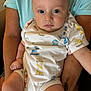 baby, infant, person, child, onesie, clothing, arms, tattoo, blue_shirt, skin, face, eyes, legs, hand, sitting, indoor, cute, calm, closeup, holding