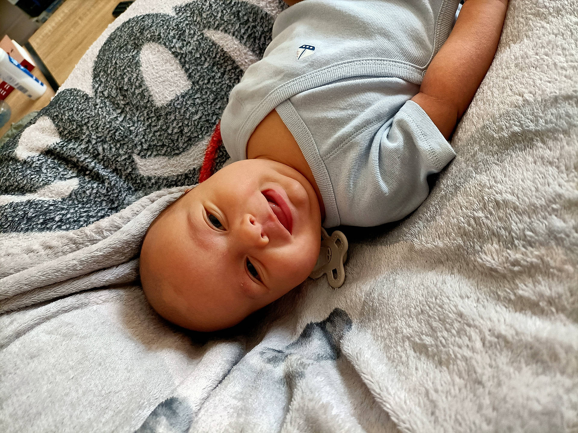 baby, blanket, child, clothing, comfort, cozy, cute, expression, face, happy, head, indoors, infant, lying_down, pacifier, resting, skin, smile, soft_texture, young