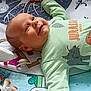 baby, smiling, infant, play_mat, toy, dinosaur, green_clothing, pacifier, colorful, child, lying_down, cute, happy, indoors, playtime, soft_toys, young_child, face, hand, reaching