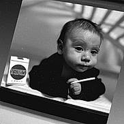 Rooster is registered to the contest to win money with this photo: baby, black_and_white, portrait, infant, candy, packaging, hand, face, shadow, monochrome, window_frame, lying_down, expression, young_child, indoor, object, person, closeup, curiosity, still_life