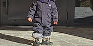 Max participe au concours pour gagner de l'argent avec cette photo : toddler, child, helmet, goggles, snowsuit, boots, outdoor, porch, stone, shadow, winter_clothing, small_person, standing, sunlight, front_door, concrete_steps, young_child, cold_weather, protective_gear, serious_expression