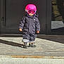 toddler, child, helmet, goggles, snowsuit, boots, outdoor, porch, stone, shadow, winter_clothing, small_person, standing, sunlight, front_door, concrete_steps, young_child, cold_weather, protective_gear, serious_expression