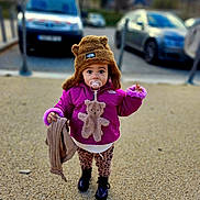 Max a rejoint le concours — aidez-le/la à gagner de superbes lots ! child, toddler, hat, jacket, pacifier, teddy_bear, blanket, outdoor, gravel, shoes, curious, cute, winter_clothing, standing, toy, person, young_child, street, daylight, cold_weather