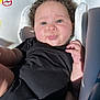 baby, black_clothing, car_seat, child, curly_hair, cushioned_seat, cute, drool, expression, face, hand, indoor, infant, legs, onesie, portrait, skin, sunlight, tongue_out, young