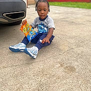 Jazier is registered to the contest to win money with this photo: blue, braided_hair, car, casual, cheetos, child, clothing, concrete, daylight, holding, orange, outdoor, pavement, person, sitting, snack, sneakers, street, toddler, young_child