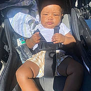 Kamari is registered to the contest to win money with this photo: baby, child, stroller, sunlight, blanket, water_bottle, clothing, socks, seatbelt, infant, outdoor, person, cute, legs, face, hands, summer, shade, resting, portrait