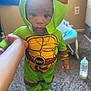 Kamari joined the competition — help win amazing prizes! toddler, child, costume, tmnt, green, yellow, baby, carpet, hand, necklace, bottle, baby_gear, indoor, person, footwear, hood, face, standing, room, toy