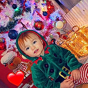Fabio a rejoint le concours — aidez-le/la à gagner de superbes lots ! child, christmas_lights, christmas_tree, cozy, curtains, elf_costume, festive_clothing, gift_boxes, gingerbread_man, glowing_lights, heart_emoji, holiday, holiday_decor, indoors, ornaments, plush_toy, red_and_white_stripes, smiling_child, toddler, wooden_floor