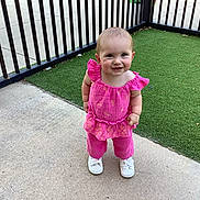 Olivia joined the competition — help win amazing prizes! toddler, child, smiling, outdoor, grass, concrete, fence, pink_clothing, white_shoes, happy, person, baby, cute, standing, daylight, portrait, young_child, casual_clothing, playful, sunlight