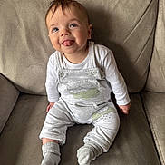 Harrison is registered to the contest to win money with this photo: baby, child, infant, smiling, tongue_out, blue_eyes, overalls, socks, couch, furniture, indoor, cute, happy, person, portrait, seated, clothing, soft_texture, comfortable, playful
