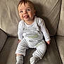 baby, child, infant, smiling, tongue_out, blue_eyes, overalls, socks, couch, furniture, indoor, cute, happy, person, portrait, seated, clothing, soft_texture, comfortable, playful