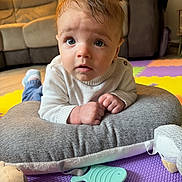 Harrison is registered to the contest to win money with this photo: baby, child, face, blue_eyes, white_sweater, cushion, toy, play_mat, indoor, living_room, carpet, expression, hands, curly_hair, soft_toys, floor, comfort, portrait, cute, curious