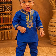 Samuel is registered to the contest to win money with this photo: toddler, child, portrait, standing, traditional_clothing, blue_outfit, embroidered_clothing, cultural_fashion, hat, cap, shoes, smiling, indoor, studio, woven_rug, decorative_basket, textile, warm_lighting, full_body, fashion_photography