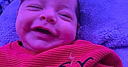 Micah joined the competition — help win amazing prizes! baby, smiling, red_sweater, indoor, purple_lighting, blanket, infant, happy, closeup, portrait, child, cozy, cute, face, hand, soft_texture, relaxed, young_child, warm_clothing, home