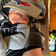 Micah is registered to the contest to win money with this photo: baby, sleeping, cap, clothing, person, arm, indoor, wooden_floor, plant, hand, face, peaceful, cozy, fabric, infant, resting, closeup, portrait, newborn, casual