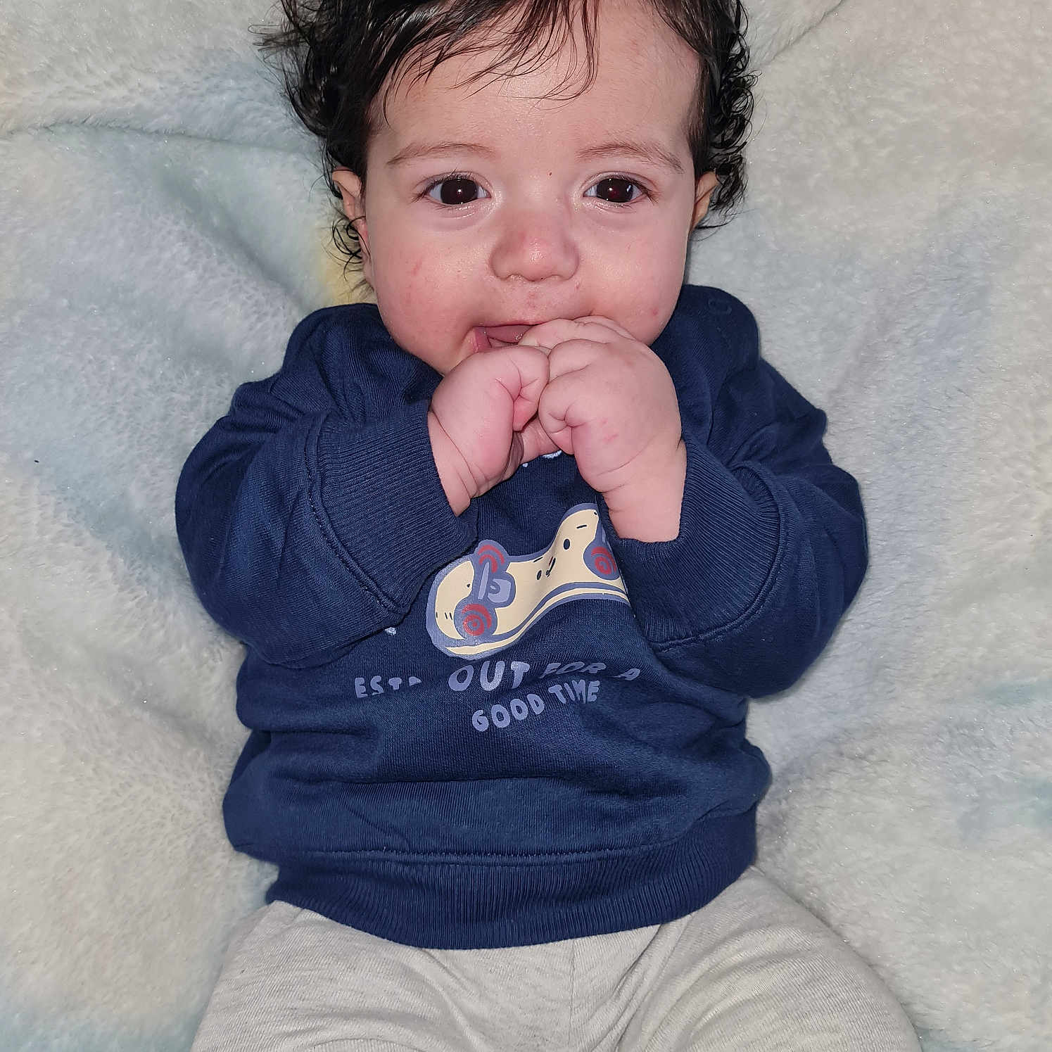Yahya a rejoint le concours — aidez-le/la à gagner de superbes lots ! baby, blanket, blue_sweatshirt, chewing, child, clothing, cozy, curly_hair, cute, face, gray_pants, hands, indoors, infant, person, portrait, sitting, smiling, soft_texture, young_child