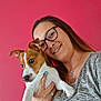 woman, dog, puppy, glasses, smile, portrait, indoor, pink_background, casual, holding, happy, young_adult, short_hair, jewelry, ring, bracelet, gray_shirt, pet, companion, friendly