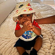 Zyair Marshall joined the competition — help win amazing prizes! baby, child, hat, nike, bucket_hat, red_shirt, black_socks, blanket, couch, indoors, curtains, window_blinds, cute, smiling, person, infant, plush, hand_to_mouth, sitting, playful