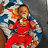 Zyair Marshall joined the competition — help win amazing prizes! baby, pacifier, red_clothing, blanket, dinosaur_pattern, cushion, child, infant, lying_down, indoors, colorful, cute, soft_toys, hands, feet, smiling, portrait, comfort, playful, resting