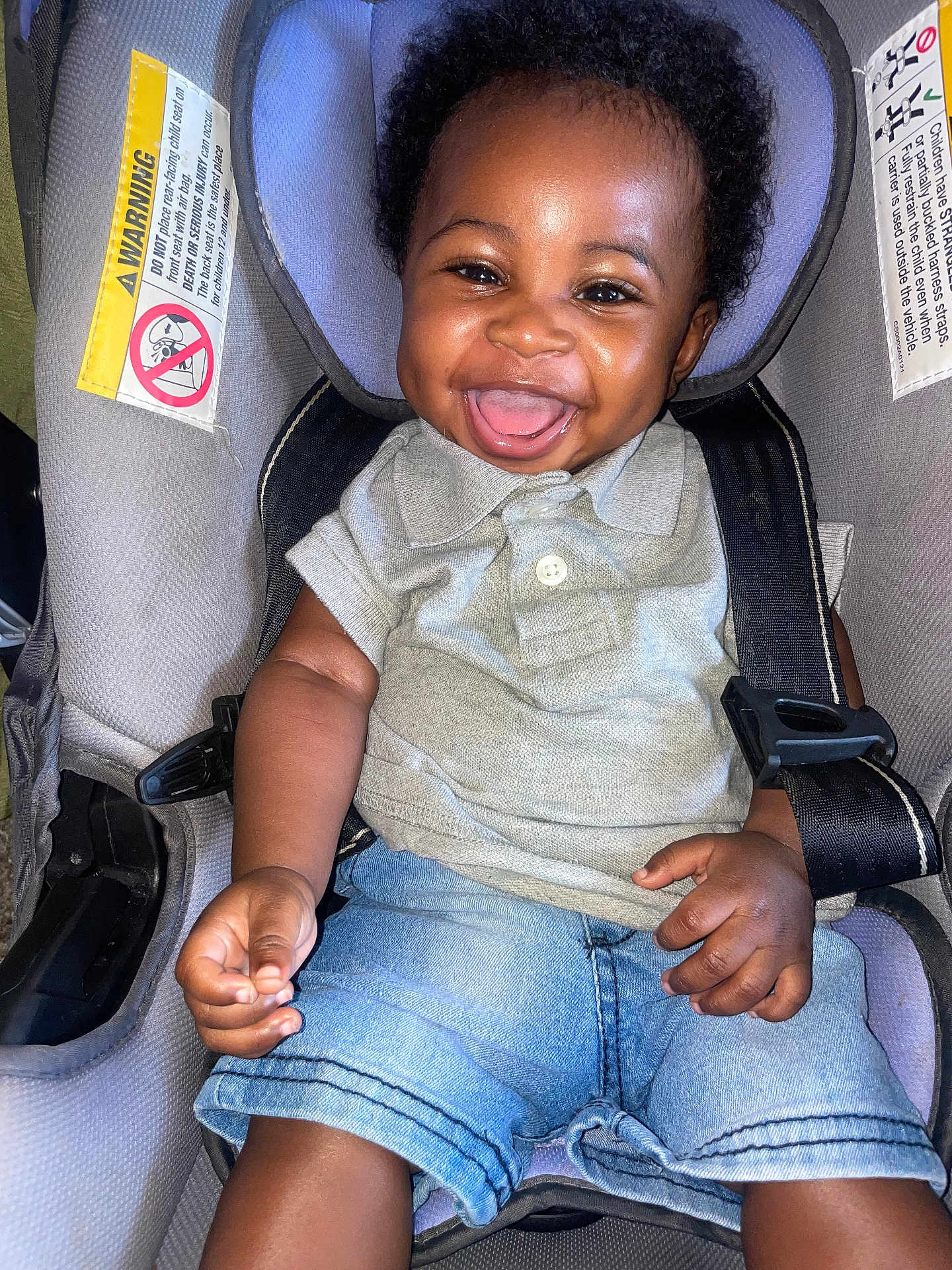 Zakari is registered to the contest to win money with this photo: baby, smiling, child, car_seat, denim_shorts, grey_polo, happy, infant, seatbelt, cute, portrait, indoors, sitting, black_hair, young, joyful, small_hands, safety, closeup, person