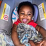 Zakari is registered to the contest to win money with this photo: baby, child, smiling, happy, blanket, car_seat, hand, comfort, toddler, infant, cute, portrait, indoor, person, clothing, pattern, fabric, skin, playful, love