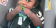 Zakari joined the competition — help win amazing prizes! baby, car_seat, child, curly_hair, toy, sneaker, clothing, straps, black_hair, hand, face, eyes, infant, seatbelt, blue_toy, cute, nibbling, indoor, sitting, child_safety