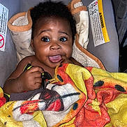 Zakari joined the competition — help win amazing prizes! baby, child, infant, blanket, car_seat, smile, happy, cute, cozy, colorful, face, hand, fingers, indoors, soft, warm, curly_hair, eyes, expression, portrait