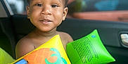 Zyaire is registered to the contest to win money with this photo: toddler, child, inflatable_floaties, yellow, green, car_interior, seat, cute, smiling, curious, baby, person, summer, water_toys, orange, octopus, hand, clothing, window, background