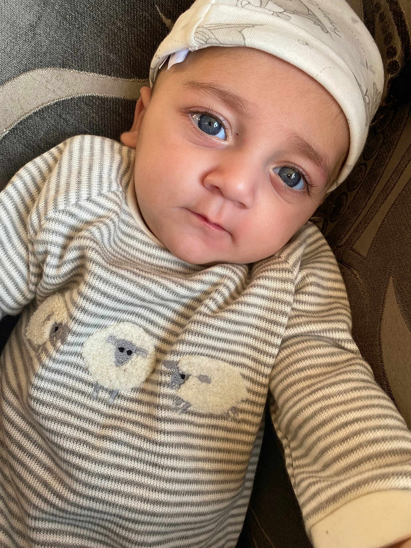 Aidan joined the competition — help win amazing prizes! baby, child, blue_eyes, striped_clothing, sheep_embroidery, cap, portrait, close_up, infant, cute, face, person, young_child, lying_down, comfort, texture, fabric, soft_lighting, indoor, expression