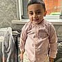 child, boy, smiling, striped_shirt, indoor, window, curtains, brick_wall, couch, blanket, patterned_wallpaper, short_hair, casual_clothing, happy, portrait, home, furniture, cozy, young, standing