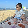toddler, child, beach, sand, sunglasses, mat, sea, sky, summer, sunny, vacation, casual_clothing, barefoot, outdoor, relaxation, people_in_background, water, shore, holiday, daytime