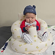 Hung Hiep Ngo is registered to the contest to win money with this photo: baby, infant, hat, blue_hat, inflatable_chair, teddy_bear_pattern, red_shirt, striped_pants, cylindrical_object, blanket, indoor, child, cute, seated, focused, person, home, cozy, comfort, young_child